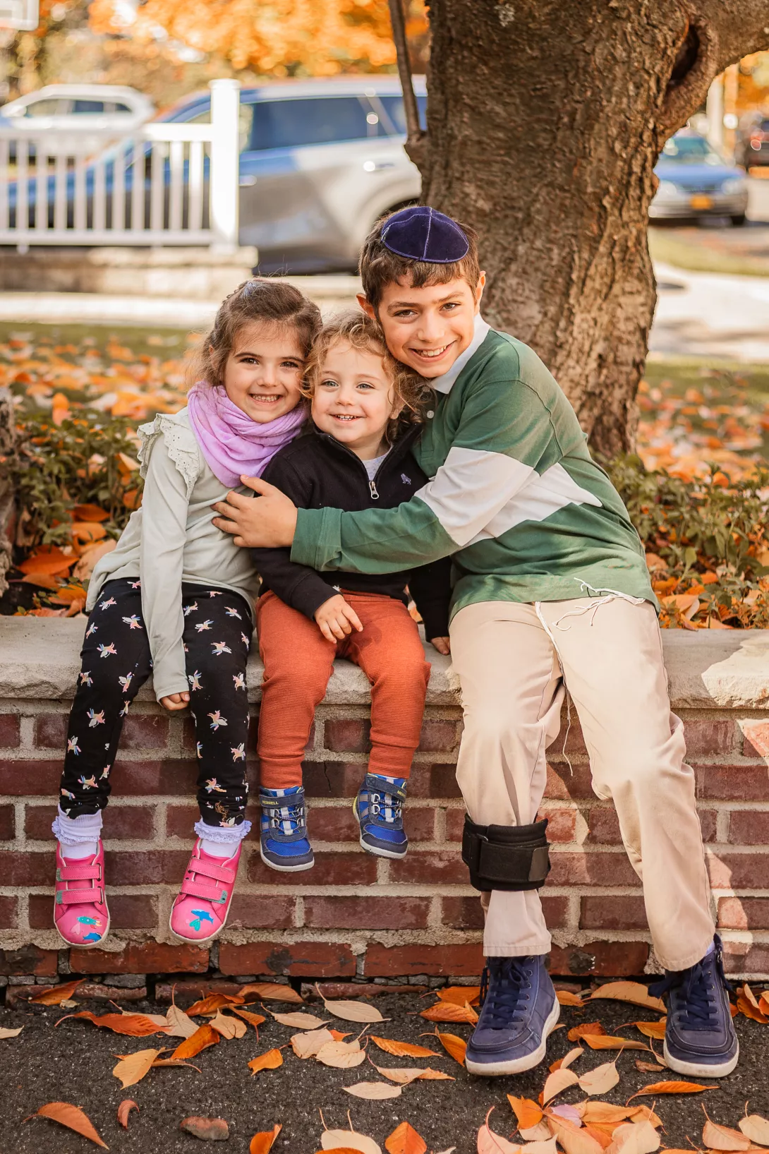 Three Jewish siblings hugging in fall leaves